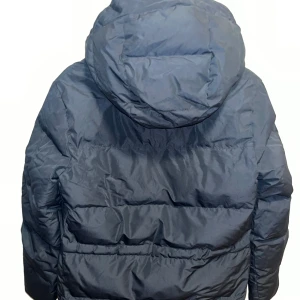 Svart  Everest pufferjacka  - Svart pufferjacka från Everest med huva och flera fickor med 2 dragkedjor. Jackan har en quiltad design och badge på ärmen. Perfekt för kalla dagar och har en riktigt skön, oversized vibe. Köpt för 1500kr har knappt använt den ser ut som ny.