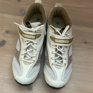 Shimano vita cykelskor med SPD-fäste - Snygga spinningskor från Shimano i vitt, guld och beige med svarta detaljer. Skorna har snörning. Knappt använda.