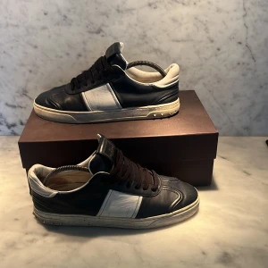 Valentino Garavani sneakers mörkblå 43EU - Snygga Valentino Garavani sneakers i svart och vitt skinn med klassisk låg profil och rund tå. Skorna har svarta snören, vita detaljer på sidorna och coola nitar på sulan. Perfekta för dig som vill ha en lyxig och stilren look med streetkänsla.