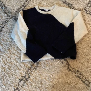 Svart och vit stickad tröja - Säljer en snygg stickad tröja i svart och vitt med coolt blockmönster. Tröjan har rund halsringning och långa ärmar, perfekt för att hålla sig varm under kyliga dagar.