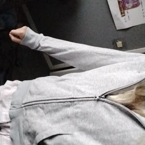 Grå hoodie från GANT med dragkedja - Säljer en stilren grå hoodie från GANT med dragkedja och huva. Tröjan har två fickor framtill och diskret GANT-logga på bröstet. Perfekt för chill dagar och enkel att matcha med det mesta. Tillverkad i mjuk bomull för skön känsla.