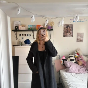 Mörkgrå kappa från Jyothi, stl 34 - Säljer en stilren mörkgrå kappa från Jyothi i storlek 34. Kappan har klassisk krage, knäppning framtill och djupa fickor. Materialet är ullblandning med slätt foder på insidan. Perfekt för dig som gillar en clean och tidlös look.