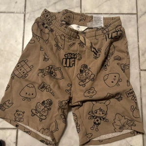 MörkBeige Toca Life x H&M shorts med print - Säljer ett par beige shorts från Toca Life x H&M med roliga tecknade figurer och snörning i midjan. Endast använd ett par gånger och inga defekter alls! Skriv om frågor osv och kolla gärna min profil❕Dessa är från några år tillbaka och finns inte längre 