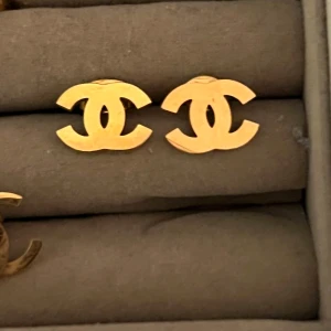 Guldiga  örhängen - Snygga örhängen . De är i guldig färg och har en stilren, ikonisk design som verkligen sticker ut. Perfekta för dig som vill ha något lyxigt och tidlöst i smyckesamlingen.