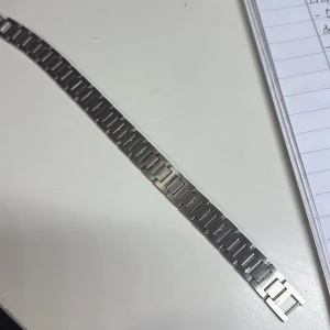 Silverfärgad klocklänk från Lacoste - Säljer en stilren klocklänk i silverfärgat metall från Lacoste. Länken har rektangulära länkar och klassisk krokodillogga på spännet. Passar dig som vill ge din klocka en sportig och modern vibe.