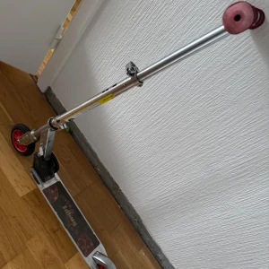 Kickbike sparkcykel - Hopfällbar kickbike med rödsvarta hjul och metallram. Handtag i röd plast, justerbar höjd. Viss yttre slitage syns på ramen och hjul, men i fullt fungerande skick. Perfekt för barn eller ungdomar för lek och transport.