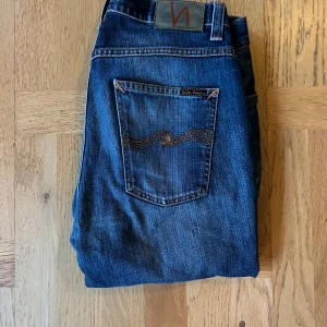 Blå jeans från Nudie Jeans - Snygga blå jeans från Nudie Jeans med klassisk femficksdesign och coola orangea sömmar på bakfickorna. Jeansen har en rak passform och är tillverkade i slitstarkt denim med snygga tvättade detaljer. Perfekt för dig som gillar stilrena och tidlösa jeans. I modell Grim Tim