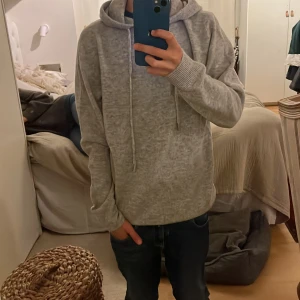 Grå hoodie i merinoull  - Säljer en chill grå hoodie med huva och snörning. Tröjan har långärmade ribbade muddar och en relaxed passform som är perfekt för att bara hänga eller dra på sig när det är lite kyligt. Enkel och stilren design som funkar till jeans eller mjukis. 