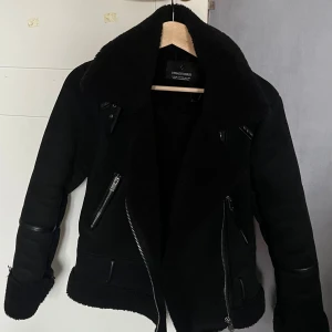 Svart teddyjacka från Stradivarius - (Utan bälte) Säljer en svart teddyjacka från Stradivarius med bred krage och detaljer i skinnimitation. Jackan har flera dragkedjor framtill, uppvikta ärmslut och en schysst oversized look. Perfekt för dig som gillar streetstyle och vill hålla dig varm.