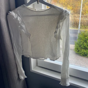 Vit  blus med volanger - Säljer en vit blus med långärmade ärmar och volangdetaljer på armarna aldrig använt 