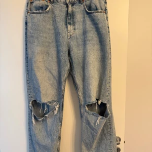 Ljusblå slitna jeans med hål på knäna - Säljer ett par ljusblå jeans med stora slitna hål över båda knäna. Klassisk femficksmodell med raka ben och vintagekänsla. Storlek 44, från Gina tricot.