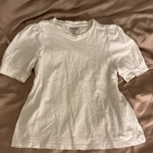 Vit blus från Aware by Vero Moda - Säljer en stilren vit blus från Aware by Vero Moda i storlek XS. Toppen har korta puffärmar och rund halsringning. Tillverkad i mjuk bomull, perfekt för en clean och fräsch look. Enkel att matcha med både jeans och kjol.