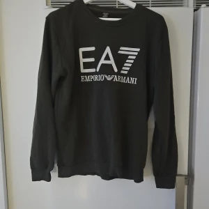 Olivgrön sweatshirt - Olivgrön sweatshirt med stor vit logga framtill. Klassisk rund halsringning och långa ärmar. Tillverkad i mjuk bomullsmix som är skön att ha på sig. Perfekt för dig som gillar stilrena och trendiga plagg med premiumkänsla. Passar även dem som har M!