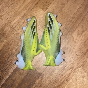 Adidas gula fotbollsskor med dobbar - Säljer ett par Adidas fotbollsskor i en cool gul färg med svarta och vita detaljer. Skorna har en strömlinjeformad design, metall- och plastdobbar för gräsplan och de klassiska tre ränderna på sidan. Ovandelen är i syntetmaterial och sulan är vit med svart mönster.