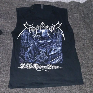 Emperor sleeveless band t-shirt - Svart ärmlös t-shirt med stort tryck av Emperor och albumet 'In The Nightside Eclipse' på framsidan. Baksidan har stor vit text med albumtiteln. Perfekt för metalheads som vill sticka ut. Materialet är mjuk bomull och passformen är normal.