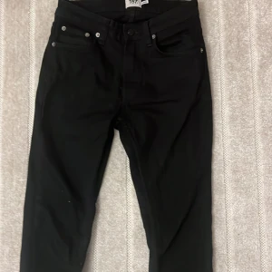 Svarta jeans från 157, storlek 28/32 - Svarta jeans från 157 med klassisk femficksdesign och silverfärgade nitar. Modellen har rak passform och normal midja. Materialet är mjukt och stretchigt jeans, vilket gör dem bekväma att bära hela dagen. Perfekt för dig som gillar stilrena och enkla svarta jeans.