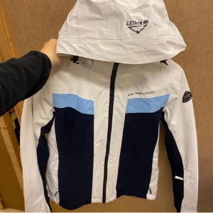 Vit och marinblå slalomjacka McKinley - Snygg slalomjacka från McKinley i vitt, marinblått och ljusblått. Jackan har huva, dragkedja framtill och coola färgblock. Pris kan diskuteras 
