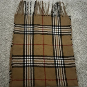 Halsduk - Snygg beige halsduk Burberry liknande med klassiskt rutigt mönster i svart, vitt och rött. Halsduken har långa fransar i ändarna och är mjuk och skön att bära. Nästan helt oanvänd❤️