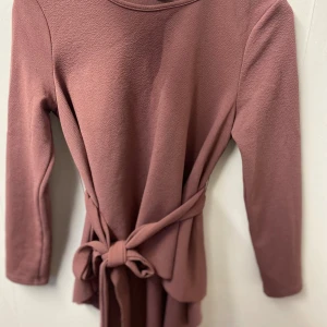 Rosa långärmad blues från SHEIN - Superfin rosa blues från SHEIN med långa ärmar och knytband i midjan. Bluesen har en enkel, stilren design och är tillverkad i ett mjukt, strukturerat material. Perfekt för dig som gillar en feminin look med snygg passform.