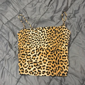 Leopardmönstrad linne från Gina Tricot - Säljer ett linne från Gina Tricot i storlek S med leopardmönster i svart och brunt. Toppen har smala axelband och är croppad i modellen. Materialet är mjukt och stretchigt