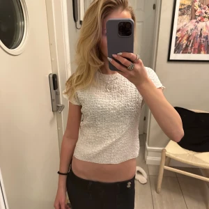 Vit croppad topp med struktur - Säljer en vit croppad topp med korta ärmar och snyggt strukturerat tyg. Toppen har en tight passform och är perfekt för dig som gillar en enkel men ändå cool stil. Passar till både jeans och kjol, och är lätt att matcha med smycken eller accessoarer.