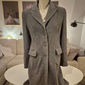 Grå ullkappa * Stl 36 * Mått i annonsen.  - Skickar gärna foton. Snygg, stilren och nätt kappa i ull från Jacqueline de Young. Danskt märke. * Storlek 36. Normal i storleken, anser jag. * Två fickor med lock. * Dekorationsknappar vid ärmsluten. * Bröst: 48 cm mätt armhåla till armhåla * Strax ovanför fickorna: 44 cm. * Nacke till ryggslut inkl krage: 101 cm * Innerärm: ca 45 cm. * Behöver sys i fodret på tre ställen. Se sista fotot. Annars i bra skick.   Djur och rökfritt hem. Se bilder och förstora då de ingår i beskrivningen.