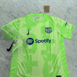 Barça Nike fotbollströja neon S - Säljer en FC Barcelona fotbollströja från Nike i neonljusgrön färg med unikt mönster. Tröjan har klubbmärke, Nike-logga och Spotify som sponsor framtill samt UNHCR-tryck bak. Tillverkad i lätt och ventilerande polyester, perfekt för match eller träning.