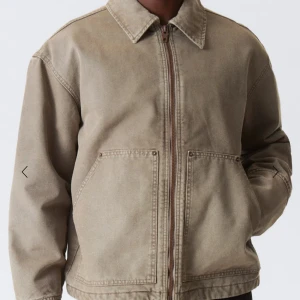  utilityjacka från Weekday - Säljer en beige utilityjacka från Weekday med klassisk krage och två stora fickor framtill. Jackan har rak passform, dragkedja och är tillverkad i bomull. Perfekt för dig som gillar en clean och chill stil.