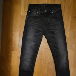 Svarta skinny jeans från Nudie W27 L30 - Snygga svarta jeans från Nudie Jeansen har slitningar och tvättade detaljer framtill och bak, samt Nudie-loggan på bakfickorna. Perfekt för dig som gillar en smal siluett och cool streetstil. Mycket bra skick