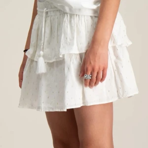 Vit Y boho frill skirt  - Superfin vit kortkjol med volanger och elastisk midja. Kjolen har dekorativa tofsar med pärldetaljer och små inslag av guldtråd i tyget som ger en extra touch. Perfekt för en somrig look och lätt att matcha med olika toppar. Från Ginatricot! Använd få ggr. ❤️