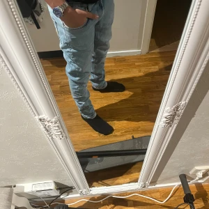 Nudie jeans med tapered fit - Säljer ett par ljusblå jeans med klassisk femficksdesign och tapered passform. Jeansen har normal midja och raka ben som smalnar av nedtill. Materialet är mjukt denim och färgen är fräsch ljusblå, perfekt för en chill och stilren look.