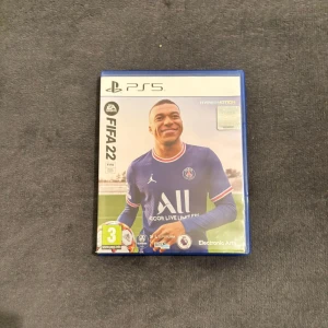 FIFA 22 PS5 - FIFA 22 till PlayStation 5 med HyperMotion-teknologi. Komplett med original fodral och skiva i mycket gott skick, utan synliga repor eller slitage. Perfekt för fotbollsälskare som vill spela med de senaste ligorna och laguppdateringarna.