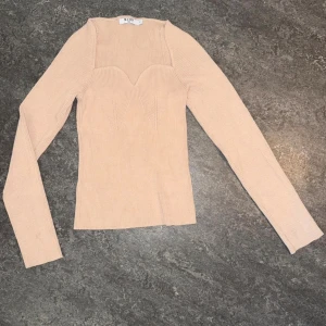 Beige ribbad långärmad topp NA-KD - Supersnygg beige ribbad topp från NA-KD med lång ärm och markerad sweetheart-detalj vid bysten. Toppen är figurnära och har en stilren, modern look som passar perfekt till jeans eller kjol.