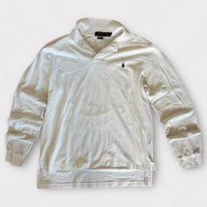 Vit långärmad pikétröja Polo Ralph Lauren - Vit långärmad pikétröja från Polo Ralph Lauren i bomull med klassisk krage och broderad marinblå logga på bröstet. Custom fit-modell med stilren look och ribbade muddar vid ärmslut. Perfekt för dig som gillar clean och tidlös stil.