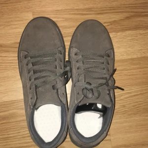 Grå mocka sneakers storlek 41 - Snygga grå sneakers i mocka med platt sula och rund tå. Skorna har snörning och diskreta vita sömmar som detalj. Insidan är fodrad i grått tyg och yttersulan är grå med mönstrad undersida för extra grepp. Perfekt för dig som gillar stilrena och enkla sneakers.