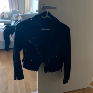 Svart jacka från ONLY, storlek 40 - Snygg svart jacka från ONLY i klassisk bikerstil. Jackan har dragkedjor framtill och vid ärmsluten, samt coola detaljer med knappar. 