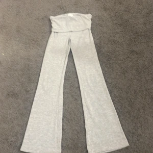 Grå mjukisbyxor från Gina Tricot - Snygga grå mjukisbyxor från Gina Tricot med hög midja och bred linning. Byxorna har ett wide snitt med utsvängda ben och är gjorda i mjukt bomullsmaterial som är superbekvämt. Perfekta för chill dagar och sköna att ha på sig hela dagen.