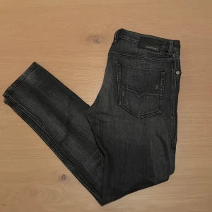 Diesel jeans - Svarta jeans från Diesel med snyggt slitna detaljer och skinny passform. Klassisk femficksdesign, låg midja och diskret logotyp på bakfickan. Jeansen är tillverkade i stretchigt denim för extra komfort och har dragkedja och knappstängning framtill.