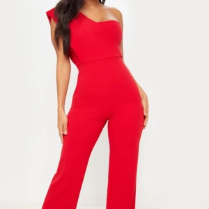 Röd one shoulder jumpsuit från PLT - Säljer en snygg röd jumpsuit med one shoulder-design och vida ben. Jumpsuiten har en figurnära passform upptill och markerad midja. Perfekt för dig som vill sticka ut med en stilren och trendig look. Materialet känns mjukt och följsamt mot kroppen. Använd en gång i tre timmar. Från Pretty Little Thing.