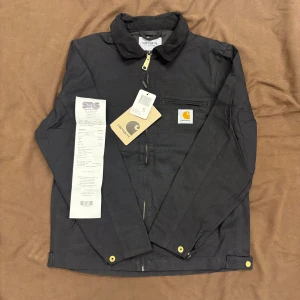 Svart Carhartt jacka - Svart Carhartt jacka som är helt oanvänd. Köpt på Naturkompaniet i våras men glömde helt att använda den så för helst tillbaka en del av pengarna så man kan droppa på lite annat. Riktigt skönt starkt material med skön insida. Carhartts klassiska tjocka dragkedja och guldknappar. Sitter riktigt bra på modellen som är 179 65kg. Skickar eller möts i Stockholm. 