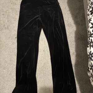 Svarta vida sammetsbyxor - Snygga svarta byxor i mjuk och glansig sammet med modellen flare. Perfekta för dig som gillar en chill och trendig look. Dessa byxor är för barn ungefär i 11 års åldern.