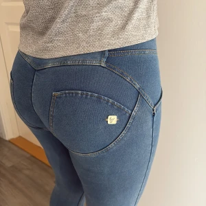 Blå tighta jeansleggings med fickdetalj - Snygga blå jeansleggings från Gina Tricot med guldfärgad logga på bakfickan och kontrastsömmar. Modellen är tight och har hög midja, vilket ger en smickrande siluett. Materialet är stretchigt och mjukt, perfekt för dig som gillar bekväma och stilrena byxor.