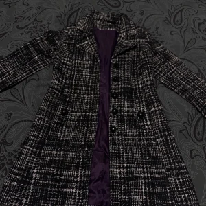 Rutig svartvit kappa från KappAhl - Säljer en snygg rutig kappa från KappAhl i svart och vitt. Jackan har stora svarta knappar, fickor framtill och ett lila innerfoder. Klassisk krage och längre modell som ger en stilren vibe. Perfekt för dig som vill sticka ut lite extra i höst och vinter. Kappans längd 87 Ärmlängd 61