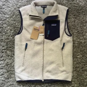 Vit fleeceväst från Patagonia - Säljer en vit fleeceväst från Patagonia med marinblå detaljer och bröstficka med. Västen är helt oanvänd och säljer den i storlek M. Kvitto med följer.
