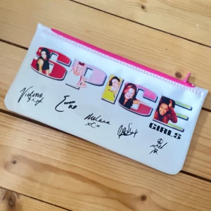 Spice Girls pennfodral  med autografer - Pennfodral i vit syntet med färgglad Spice Girls-tryck och tryckta autografer på framsidan. Väskan har en rosa dragkedja och är platt i formen, perfekt för småsaker eller som cool accessoar. Ikonisk design för dig som älskar 90-tals popkultur.
