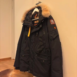 Svart Parajumpers vinterjacka XL - Snygg och varm svart Parajumpers vinterjacka i storlek XL. Klassisk modell med pälsfodrad huva, orangea detaljer och flera praktiska fickor. Jackan har det ikoniska Parajumpers-emblemet på ärmen och en robust dragkedja på insidan. Passar perfekt för kalla vinterdagar samtidigt som den ger en stilren och modern look. I mycket bra skick – välvårdad och utan skador eller fläckar. Nypris ca 10 000 kr.  Perfekt för dig som vill ha en jacka med både funktion och stil!   KAN ACCEPTERA PRISFÖRSLAG