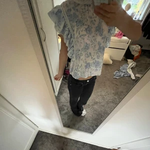 Blommig volangblus från Gina Tricot XS - Supersöt oanvänd blus från Gina Tricot i vitt med blått blommönster. Blusen är i storlek xs och har volangdetaljer längs axlarna, spetskant vid halsen och är ärmlös. 