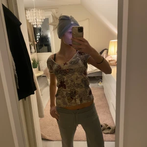 Beige ribbad topp med fjärilar från Odd Molly - Superfin beige ribbad topp från Odd Molly med v-ringning och spetskant. Toppen har ett detaljerat fjärilsmönster i rött, lila och brunt samt blommor över hela tyget. Kortärmad och figurnära passform, perfekt för dig som gillar unika prints.