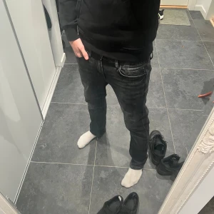 Baggy Svart/grå jeans  - Säljer ett par svarta jeans från Smog/Denim i storlek 28/30. De har klassisk femficksdesign, raka ben och normal passform. Jeansen är tillverkade i denim och har snygga slitningar för en cool look. Perfekt för dig som gillar stilrena och enkla jeans.