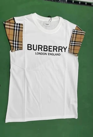 Vit  t-shirt med rutiga ärmar - Vit t-shirt  med klassiska rutiga ärmar i beige, svart och rött. Stor svart logga framtill med text. T-shirten har rund hals och är tillverkad i mjuk bomull.